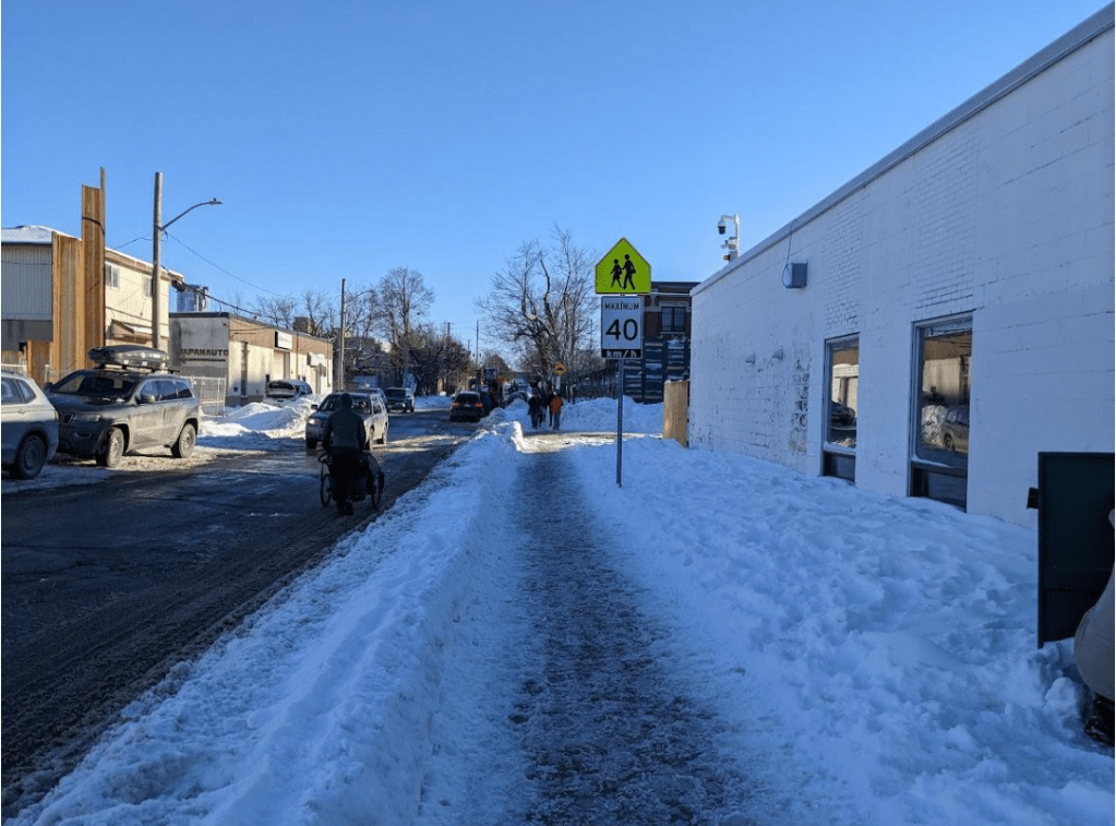 A parent pushes a stroller on the road as others walk on the sidewalk